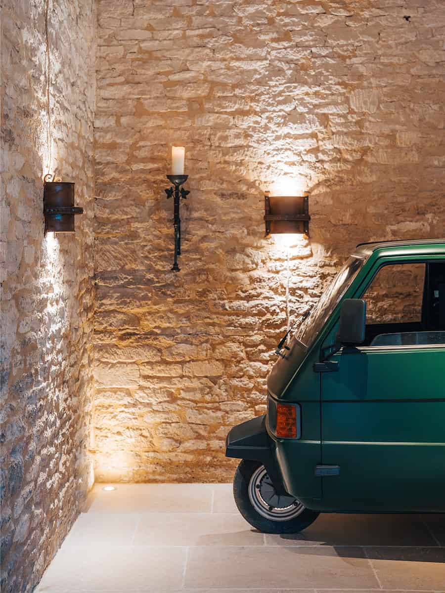 Ivy Lodge restored barn interior with Cotswolds stone walls, vintage Piaggio Ape, and wrought-iron wall sconces